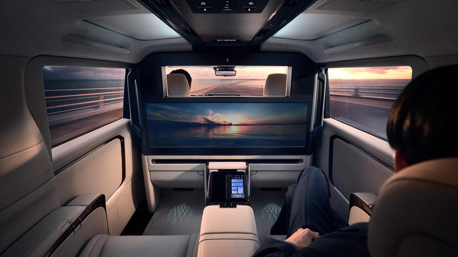 Wide interior view from the rear passenger seat. The screen is lit up and the sun is setting outside.