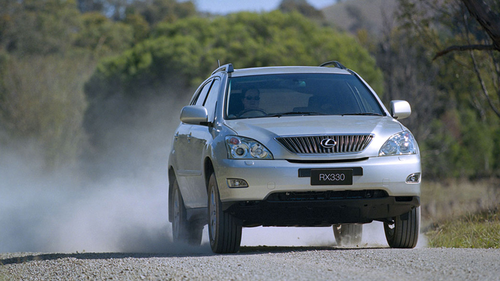 A silver Lexus SUV driving down a gravel road