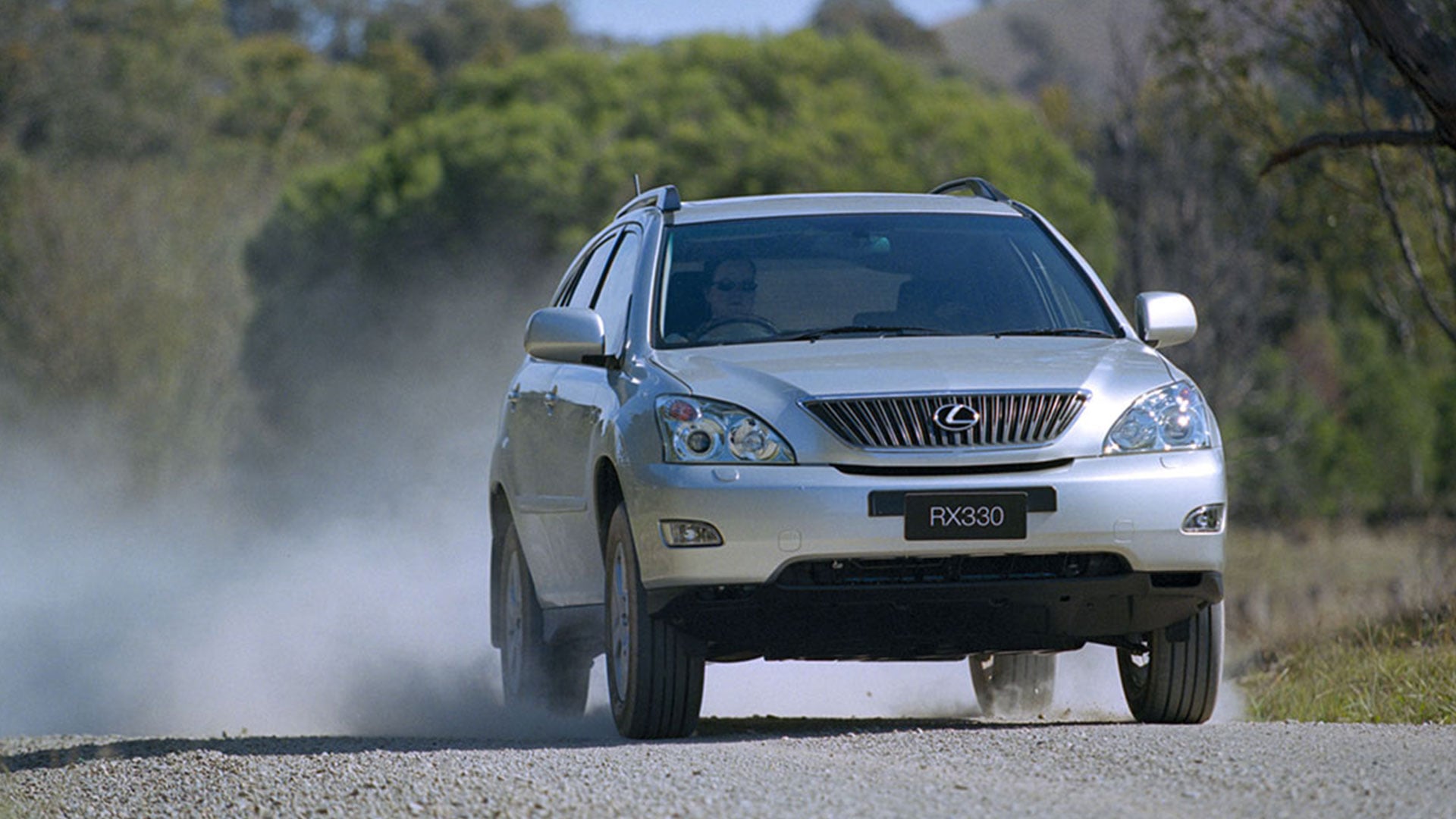 A silver Lexus SUV driving down a gravel road