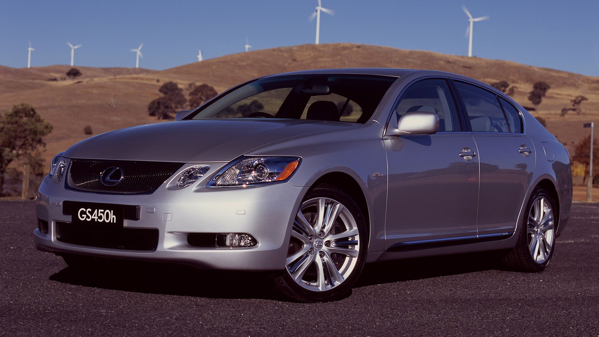 Silver Lexus GS450h sedan parked in rural landscape wind turbines in the background.